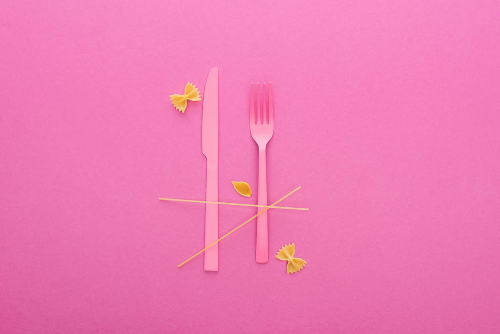 roze kunststof mes en vork, spaghetti, ongekookte Farfalle pasta en shell macaroni geïsoleerd op roze - Foto, afbeelding