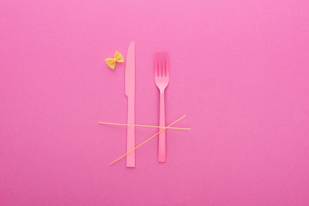 ροζ πλαστικό μαχαίρι και πιρούνι, σπαγγέτι και άψητα μακαρόνια που απομονώνονται σε ροζ - Φωτογραφία, εικόνα