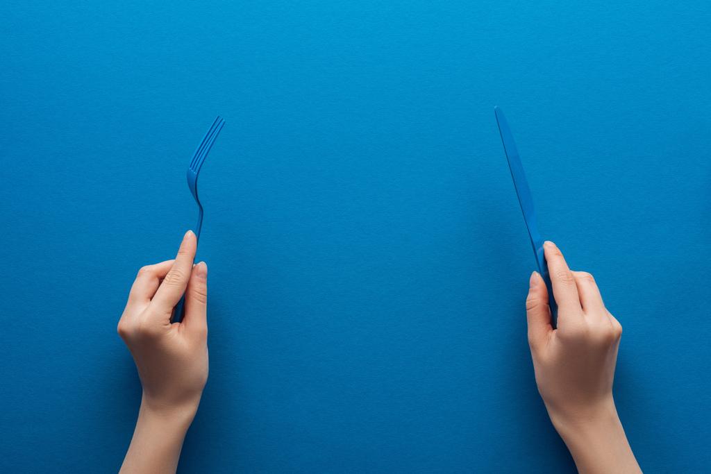 cropped view of woman holding blue plastic fork and knife on blue background - Photo, Image