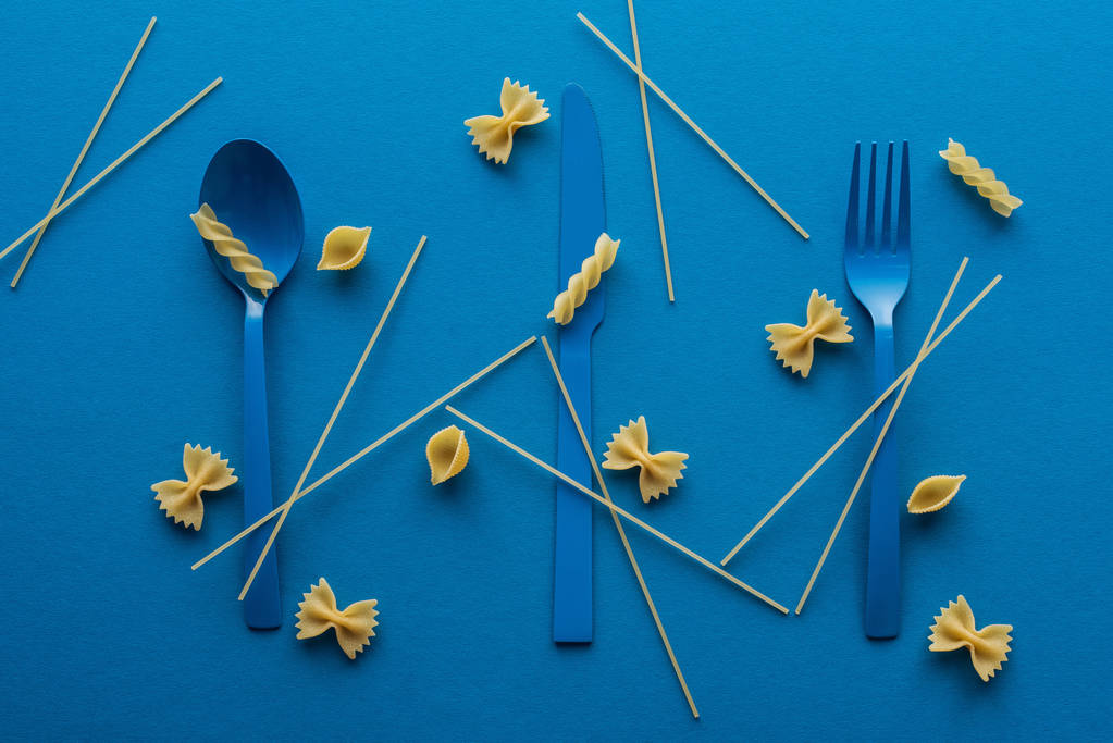 etrafında pişmemiş spagetti ve mavi arka plan makarna farklı türde mavi plastik çatal - Fotoğraf, Görsel