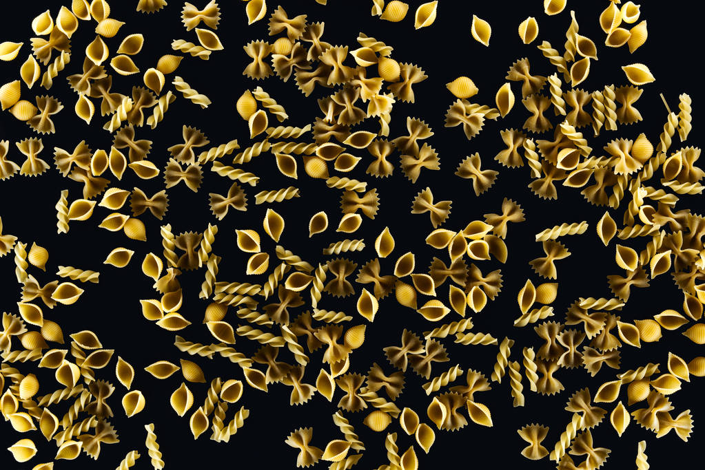 Top uitzicht van gemengde ongekookte pasta geïsoleerd op zwart  - Foto, afbeelding