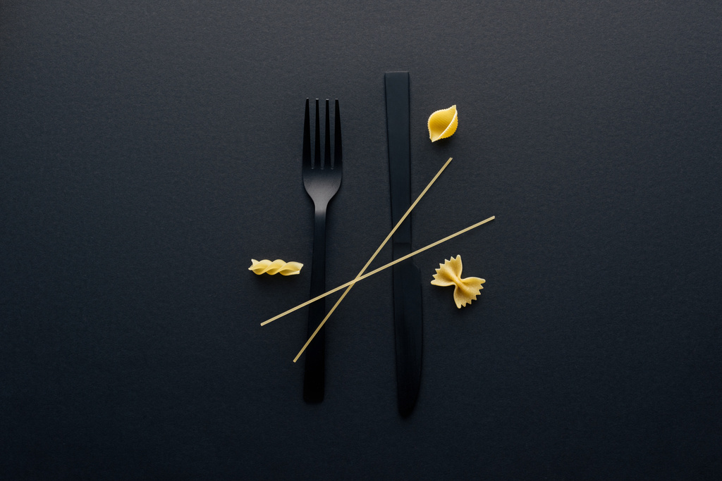 couteau en plastique noir à l'envers, fourchette et quatre différents types de pâtes sur fond noir
 - Photo, image
