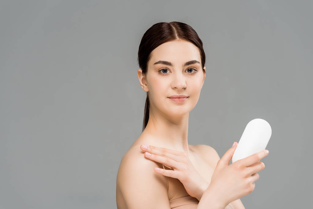 attraktive junge Frau hält Flasche mit Körperlotion isoliert auf grau  - Foto, Bild