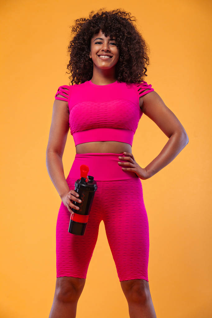 sportlich fitte Frau, Athletin mit Shaker nach dem Fitnesstraining auf gelbem Hintergrund. Fitness und Arbeitsmotivation. - Foto, Bild