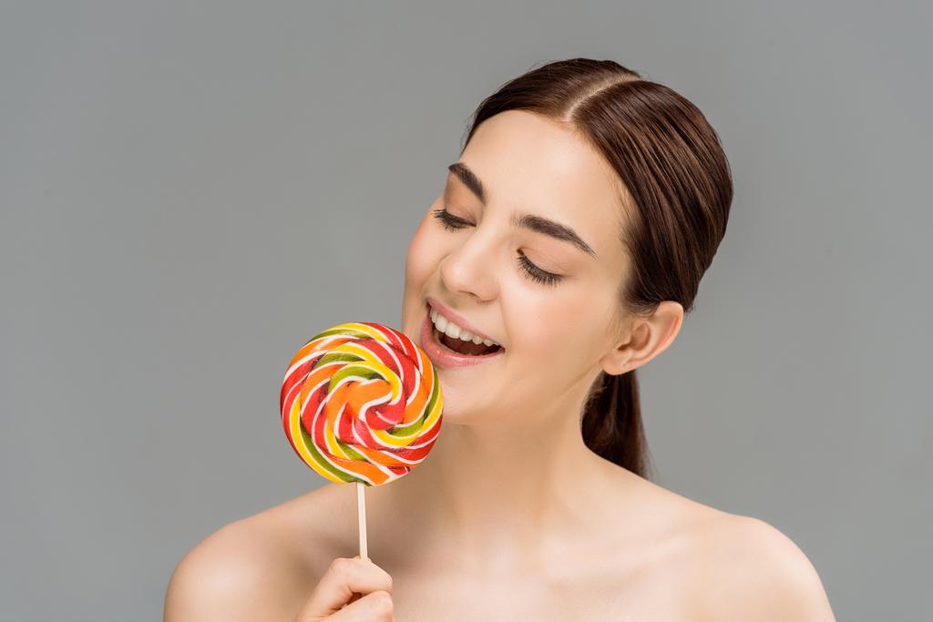 cheerful young woman looking at colorful lollipop isolated on grey  - Photo, Image