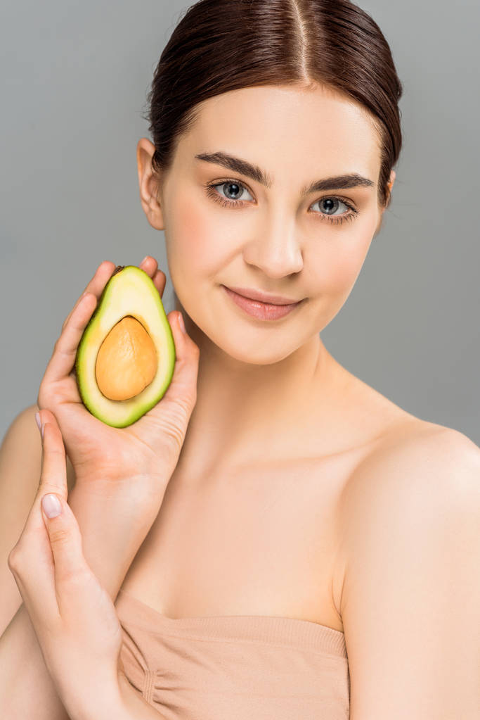 усміхнена молода жінка тримає половину авокадо ізольовано на сірому
  - Фото, зображення