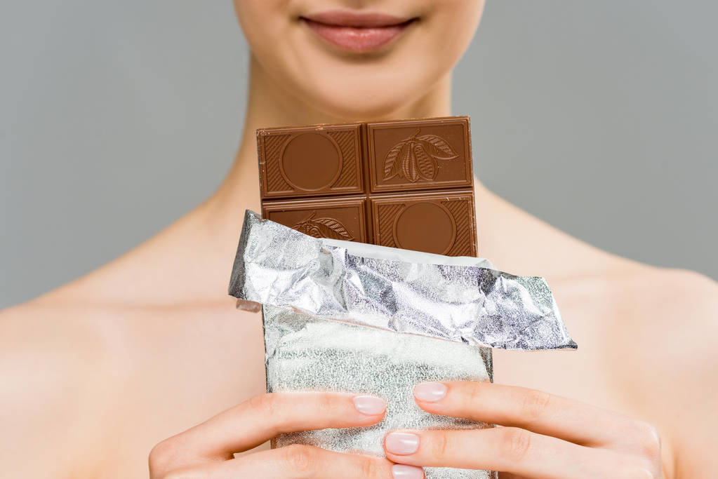 cropped view of cheerful young woman holding chocolate bar isolated on grey  - Photo, Image