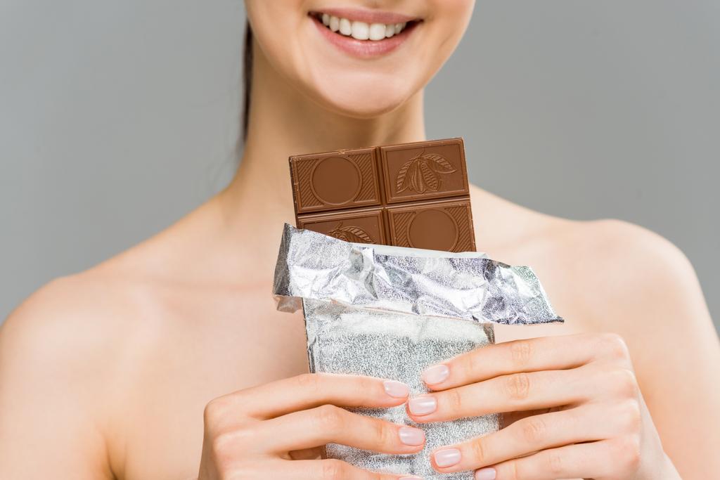 vista recortada de la joven sonriente sosteniendo barra de chocolate aislado en gris
  - Foto, Imagen
