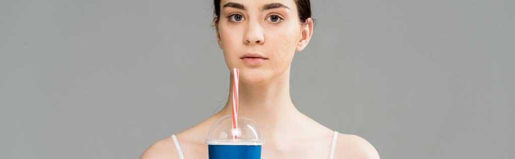 Panoramaaufnahme einer jungen Frau mit Problemhaut, die Plastikbecher isoliert auf Grau hält  - Foto, Bild