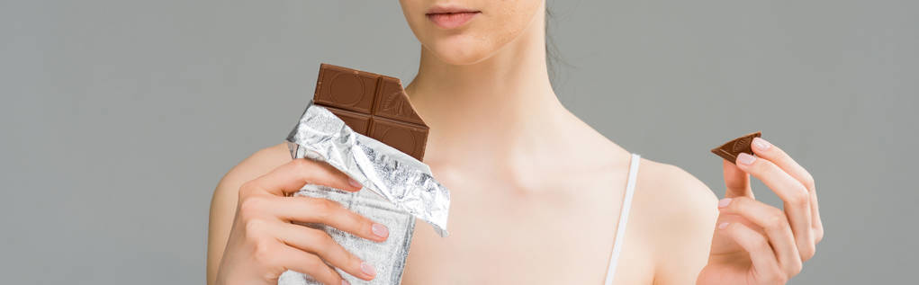 plan panoramique de la jeune femme avec la peau problème tenant barre de chocolat et regardant la caméra isolée sur gris
  - Photo, image