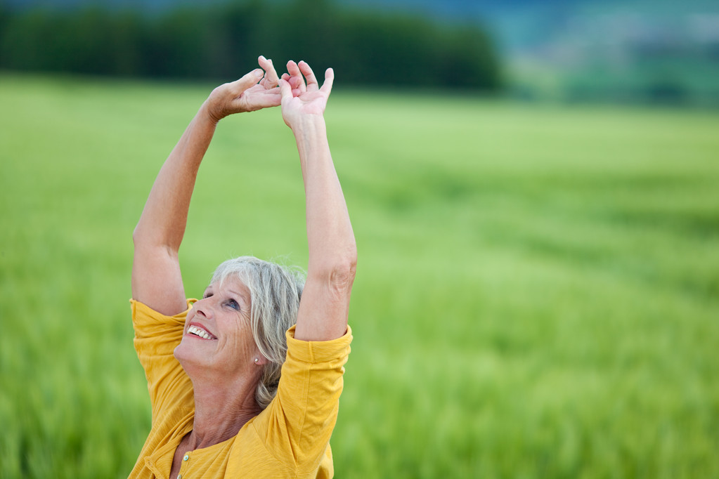 Mulher sênior com braços levantados olhando para cima no campo gramado
 - Foto, Imagem