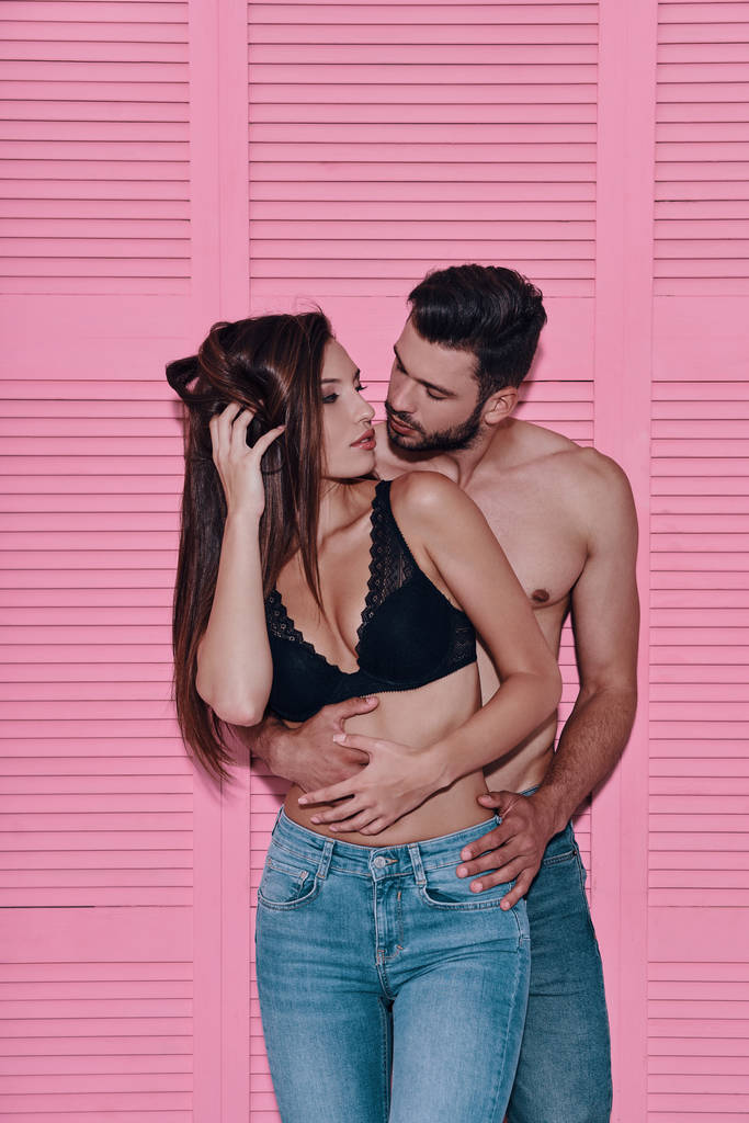 Красива молода пара обіймається, стоячи на рожевому фоні
      - Фото, зображення