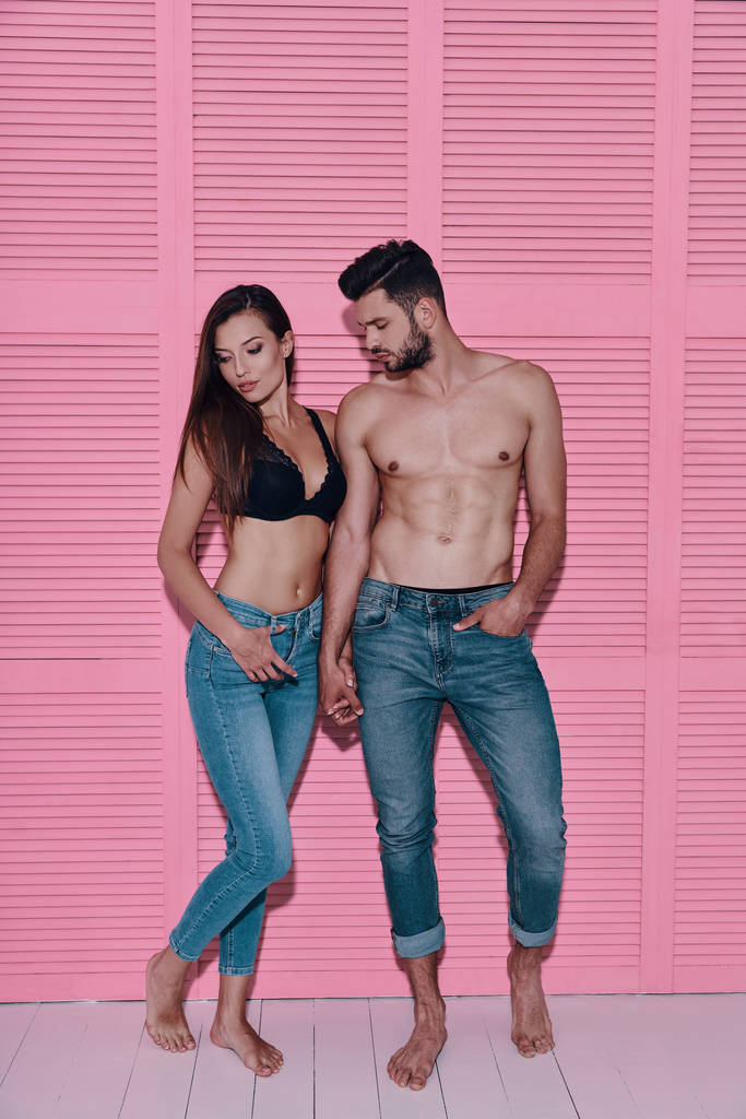 Longitud completa de hermosa pareja joven cogida de la mano mientras está de pie sobre el fondo rosa
 - Foto, imagen