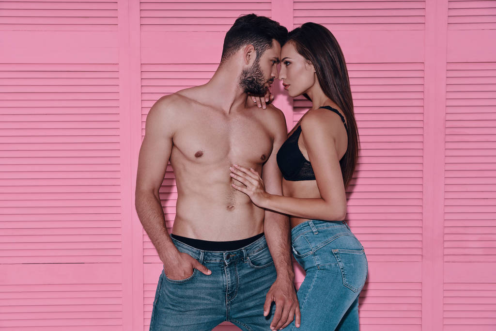 Bella giovane coppia legame faccia a faccia mentre in piedi contro sfondo rosa
           - Foto, immagini