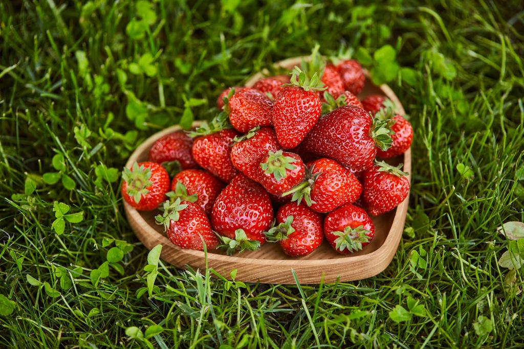 frische Erdbeeren in herzförmigem Holzteller auf grünem Gras  - Foto, Bild