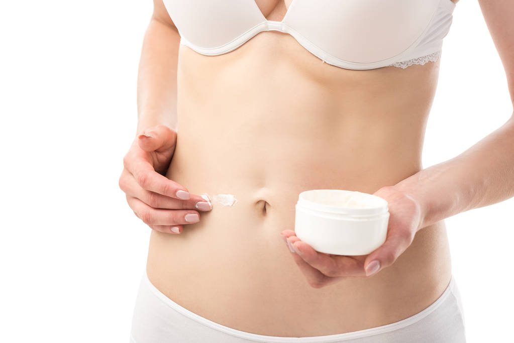 обрезанный вид молодой женщины в нижнем белье нанесение косметического крема на живот изолированы на белом
 - Фото, изображение