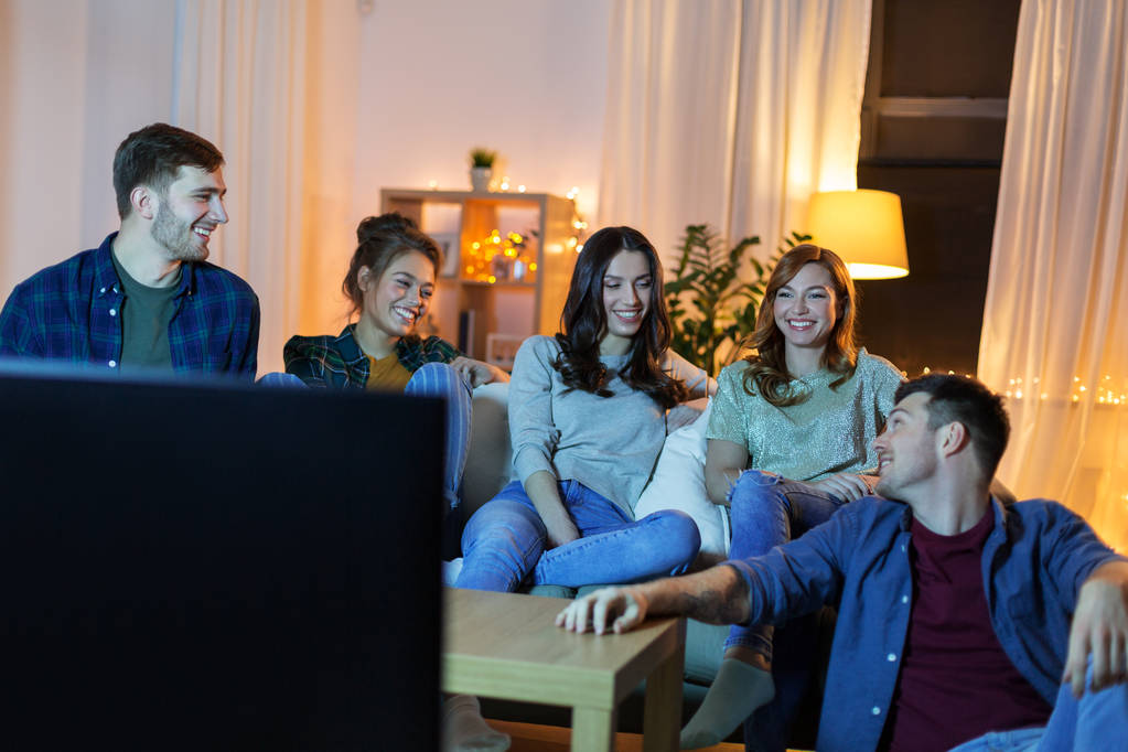 onnellisia ystäviä katsomassa televisiota kotona illalla
 - Valokuva, kuva