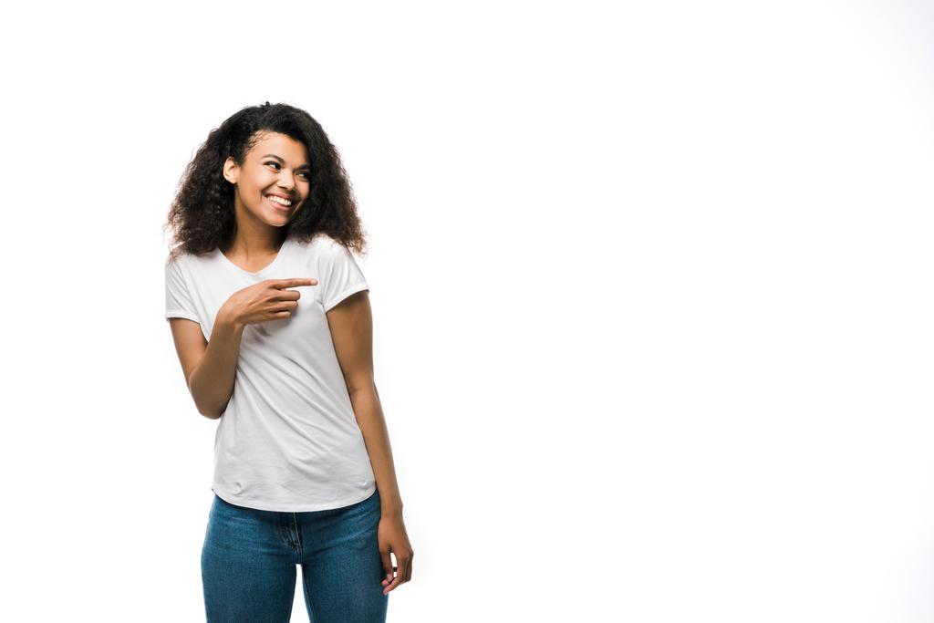 白いTシャツを着た幸せなアフリカ系アメリカ人の女の子は、白で孤立した青いジーンズに立っている間、指で指を指さす  - 写真・画像