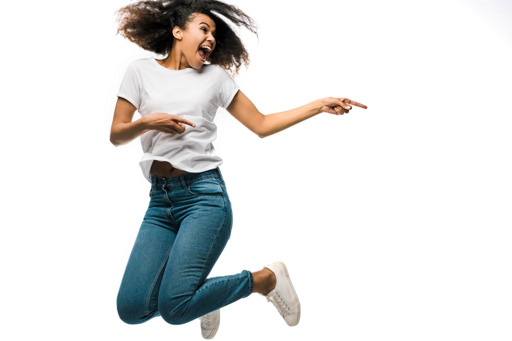 vrolijke Afro-Amerikaanse vrouw wijzend met vingers en springen geïsoleerd op wit  - Foto, afbeelding