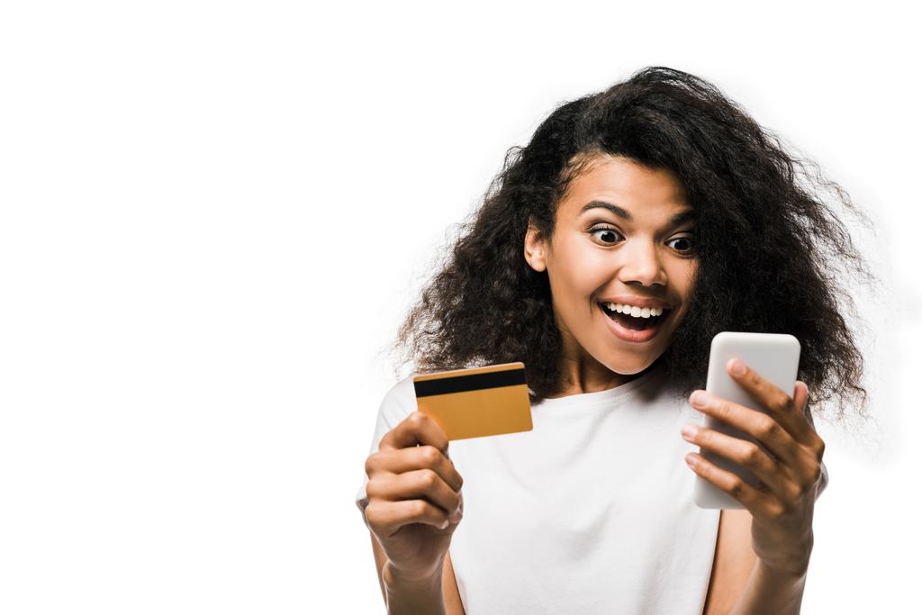 alegre afroamericana mujer sosteniendo tarjeta de crédito y mirando el teléfono inteligente aislado en blanco
  - Foto, Imagen