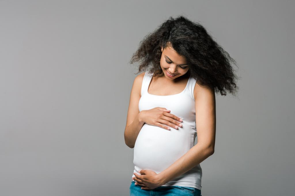 feliz embarazada africana americana chica tocando vientre en gris
  - Foto, Imagen
