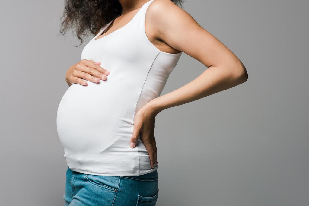 περικομμένη θέα της νεαρής έγκυος αφρικανική αμερικανική γυναίκα αγγίζοντας την κοιλιά σε γκρι  - Φωτογραφία, εικόνα