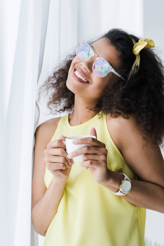 mujer afroamericana feliz en vasos sosteniendo taza con bebida
  - Foto, Imagen
