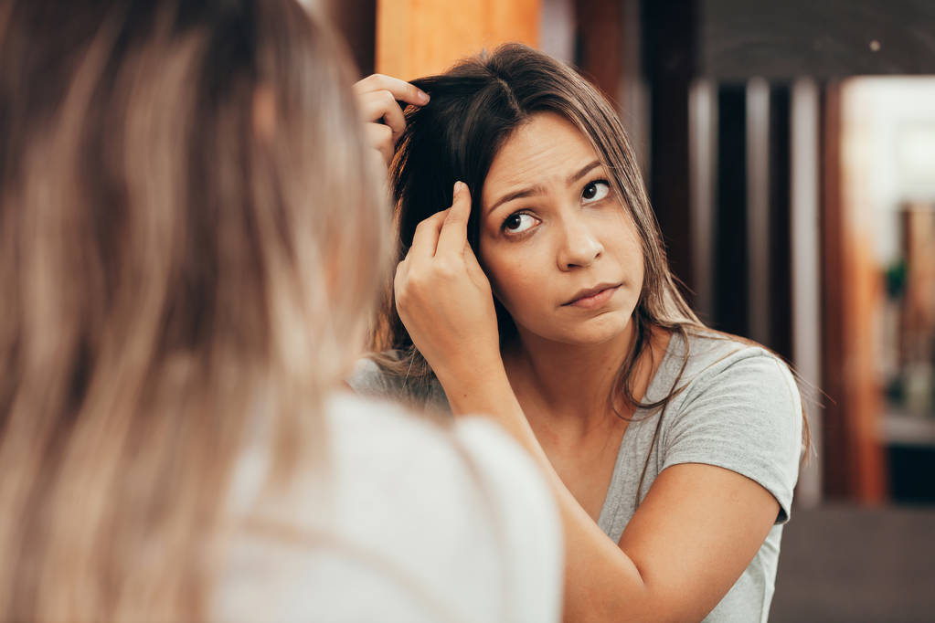 Молодая женщина с проблемой выпадения волос, глядя в зеркало дома
 - Фото, изображение