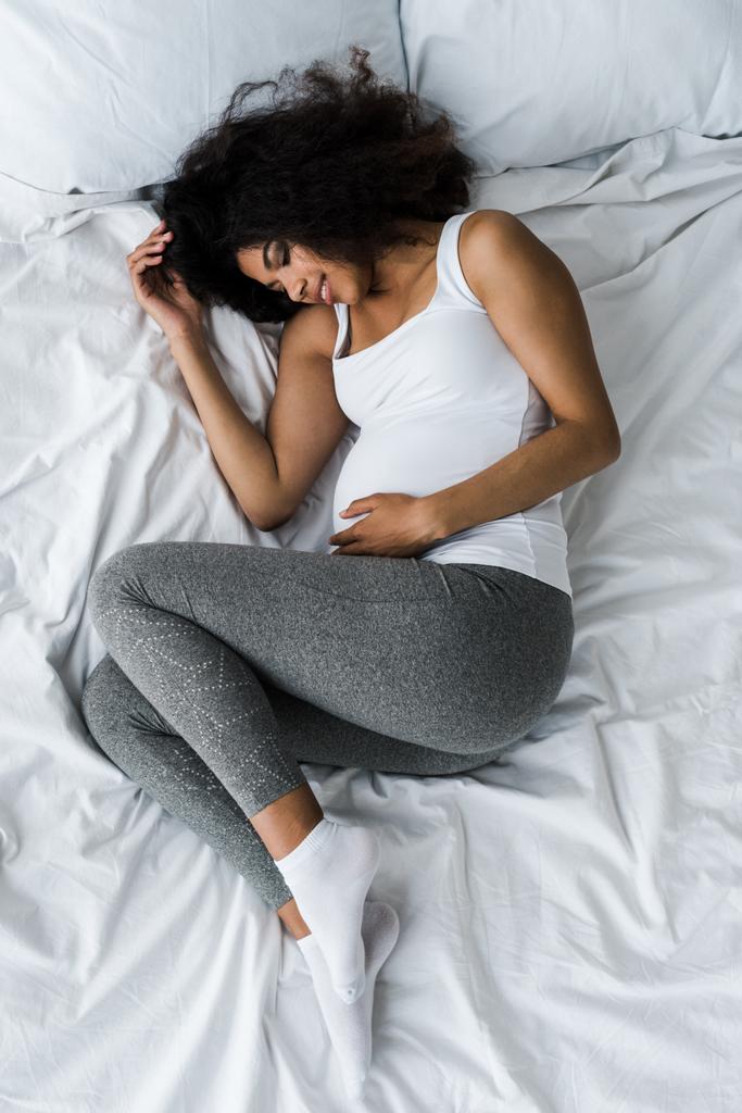 vista dall'alto della donna africana americana incinta con gli occhi chiusi sdraiati sul letto
  - Foto, immagini