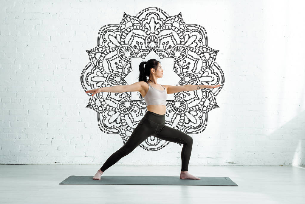calma donna asiatica in piedi con le mani tese su tappetino yoga vicino ornamento mandala
  - Foto, immagini