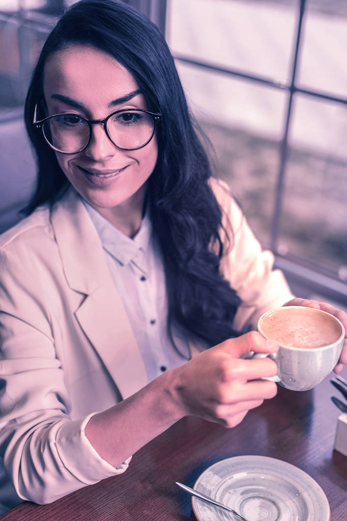 Morgengetränk. positive kluge Geschäftsfrau hält morgens eine Tasse Cappuccino in der Hand, während sie ihn trinkt - Foto, Bild