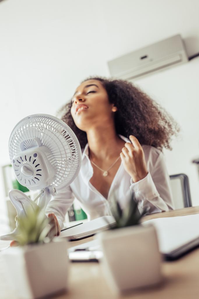 foyer sélectif de femme d'affaires afro-américaine tenant ventilateur électrique tout en souffrant de chaleur au bureau
 - Photo, image