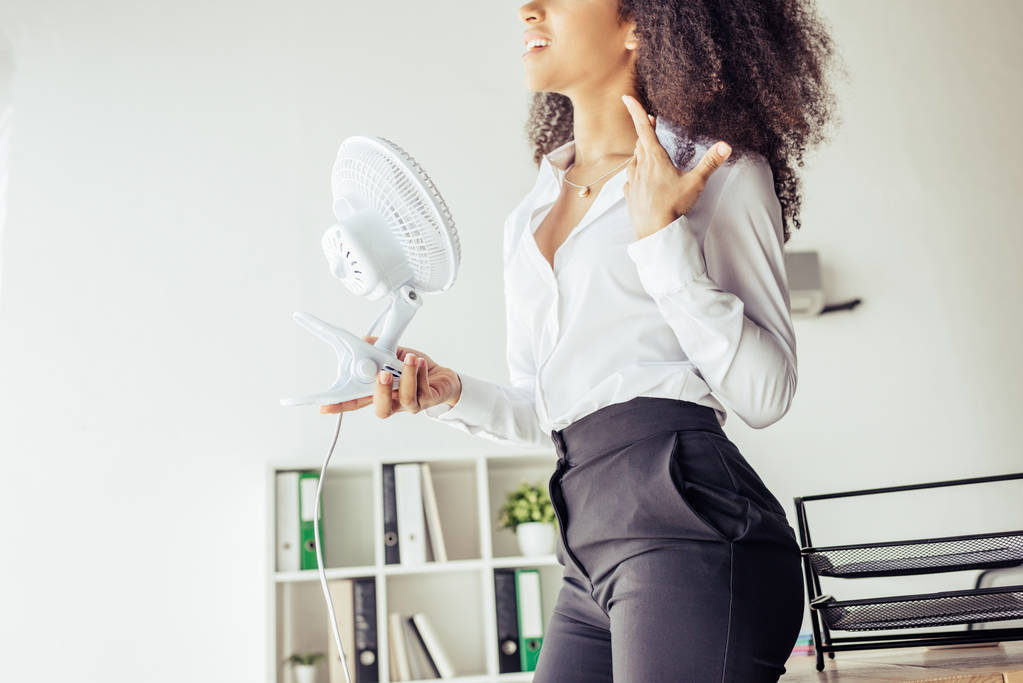 částečný pohled na Africkou americkou ženu, která drží ventilátor a zároveň trpí teplem v úřadu - Fotografie, Obrázek