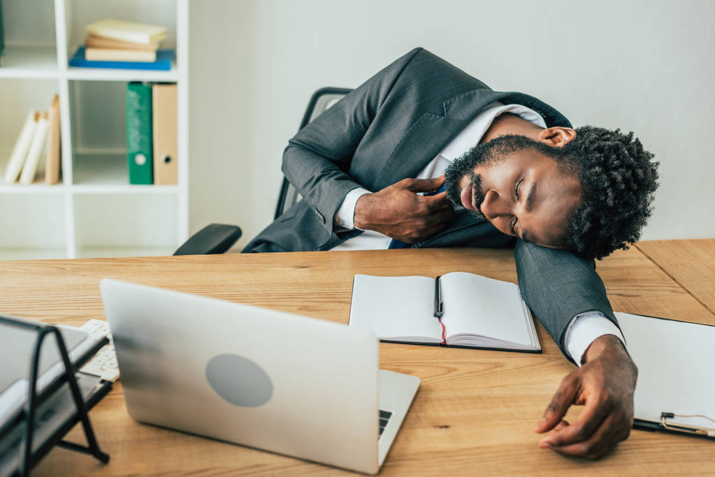 agotado hombre de negocios afroamericano acostado en el escritorio mientras sufría de calor de verano en la oficina
 - Foto, imagen