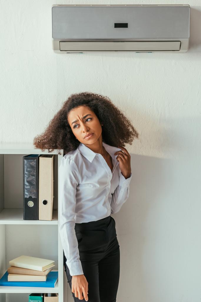 donna d'affari africana americana insoddisfatta in piedi sotto il condizionatore d'aria e distogliendo lo sguardo
  - Foto, immagini