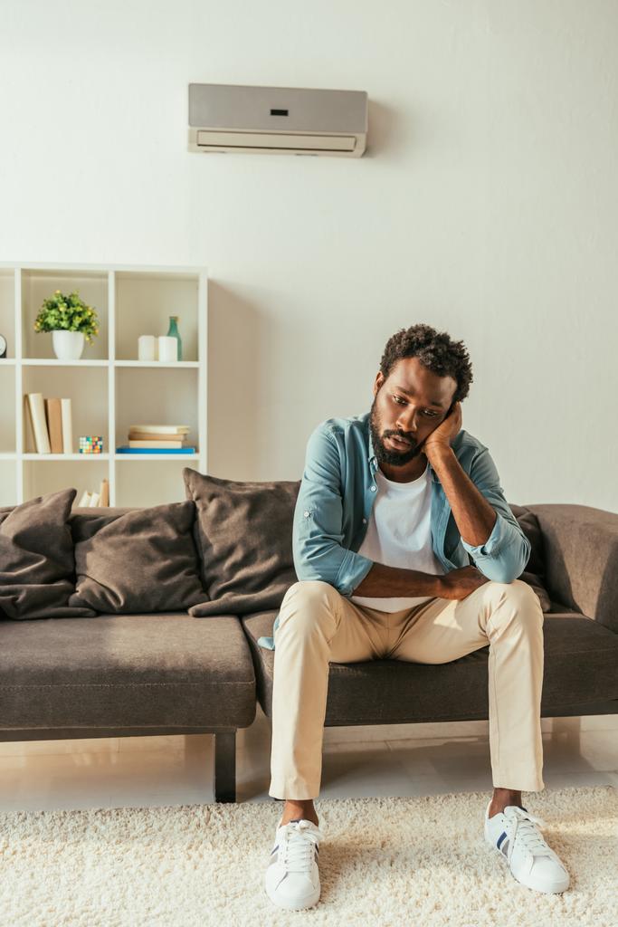kimerült afro-amerikai ember szenved nyári melegben ülve a kanapén otthon - Fotó, kép