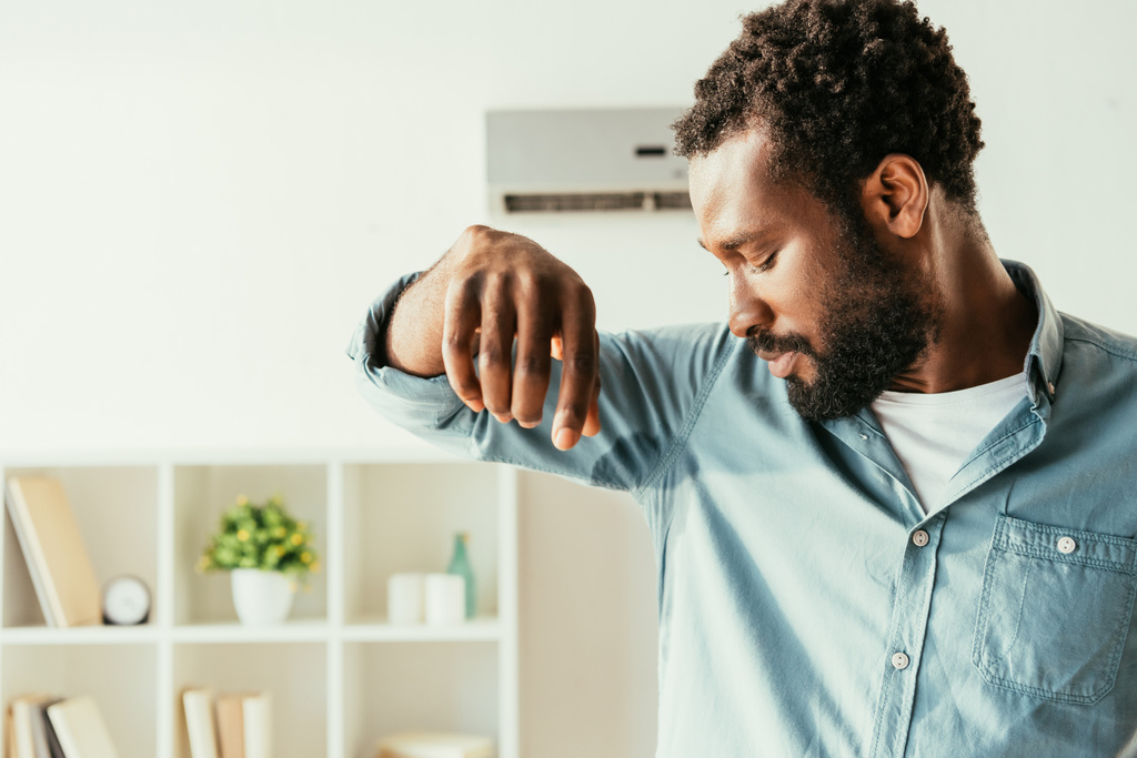 elégedetlen afro-amerikai férfi nézi izzadt inget, miközben szenved hőt otthon - Fotó, kép