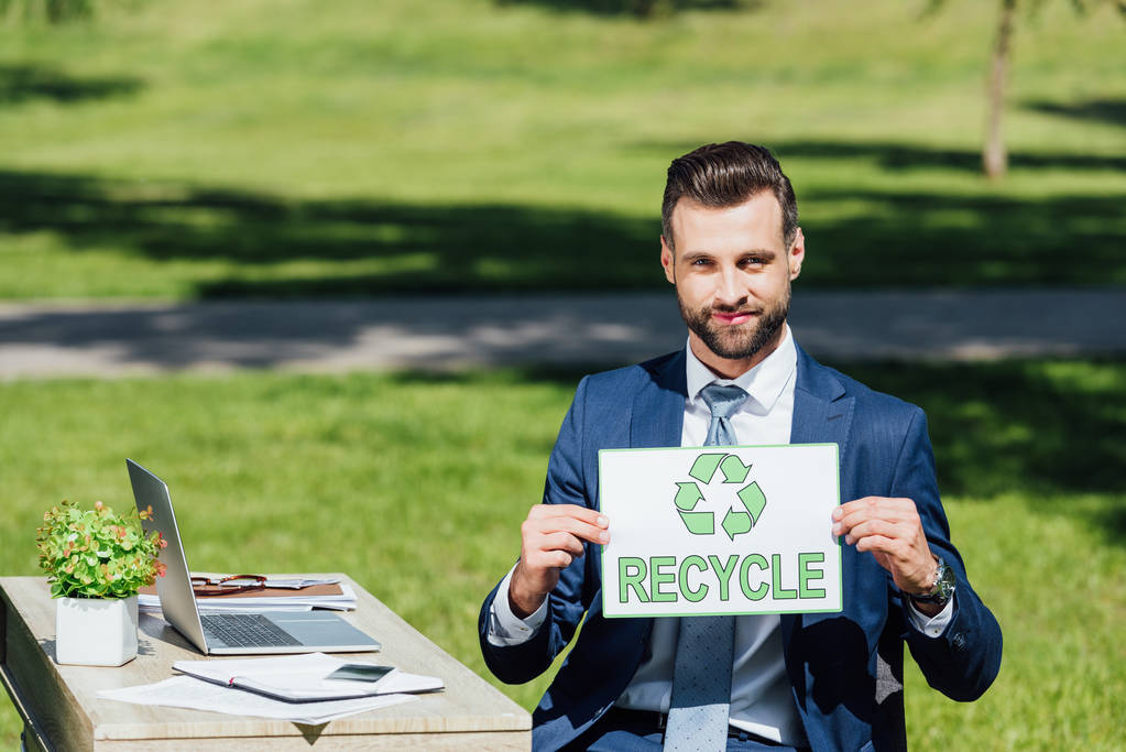 zakenman zit in de buurt van tafel en toont kaart met recycle belettering - Foto, afbeelding