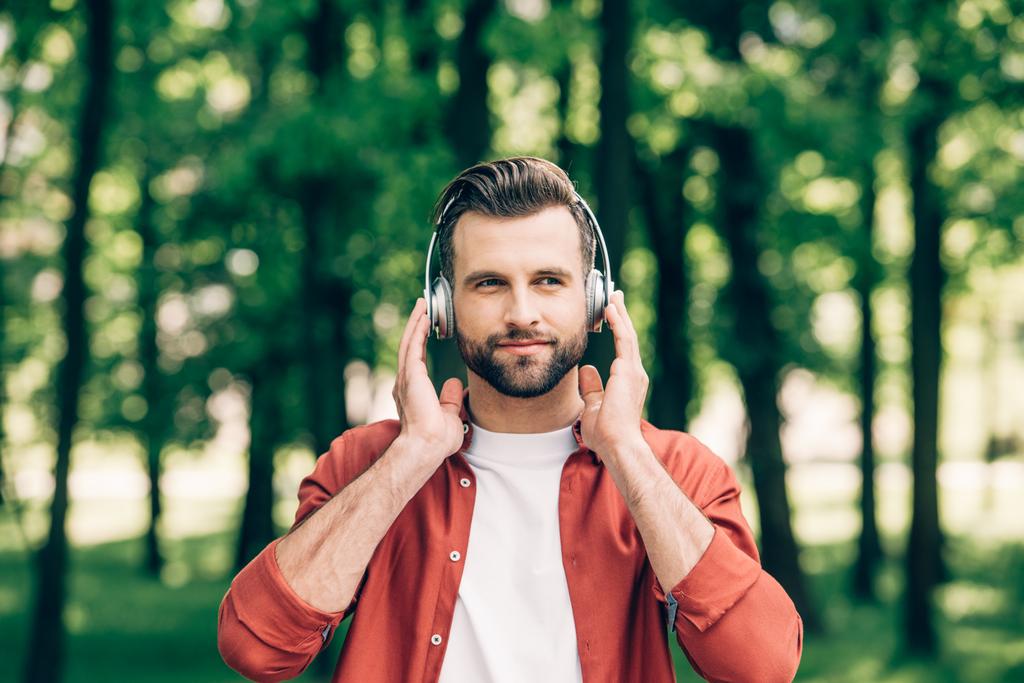 young man standing in park, listening to music and looking away - Photo, Image