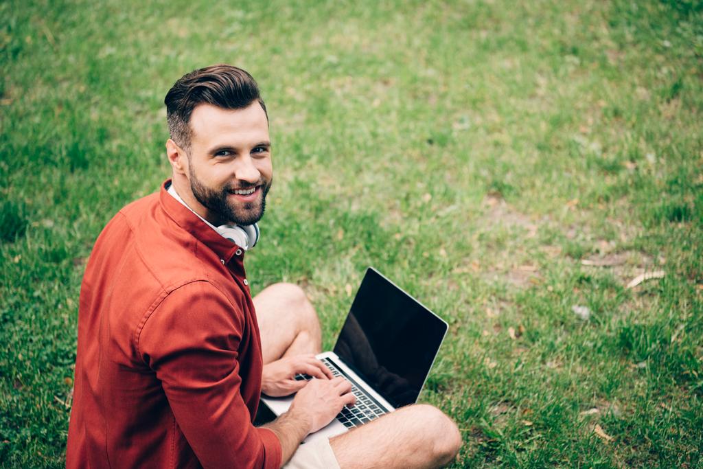 ノートパソコンを使用して赤いシャツを着た男、笑顔とカメラを見て - 写真・画像