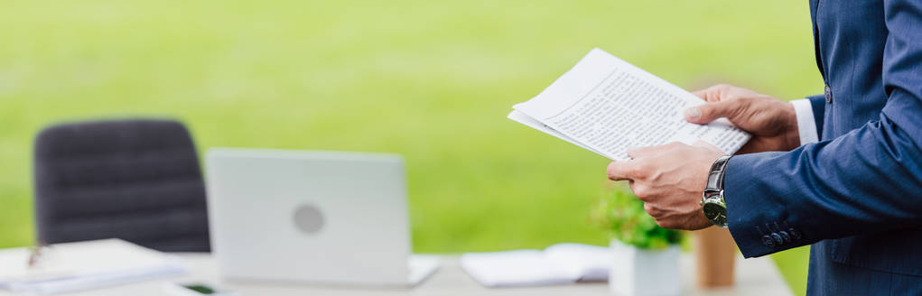 panoramic shot of man holding newspaper in park near white table with office stuff - Photo, Image