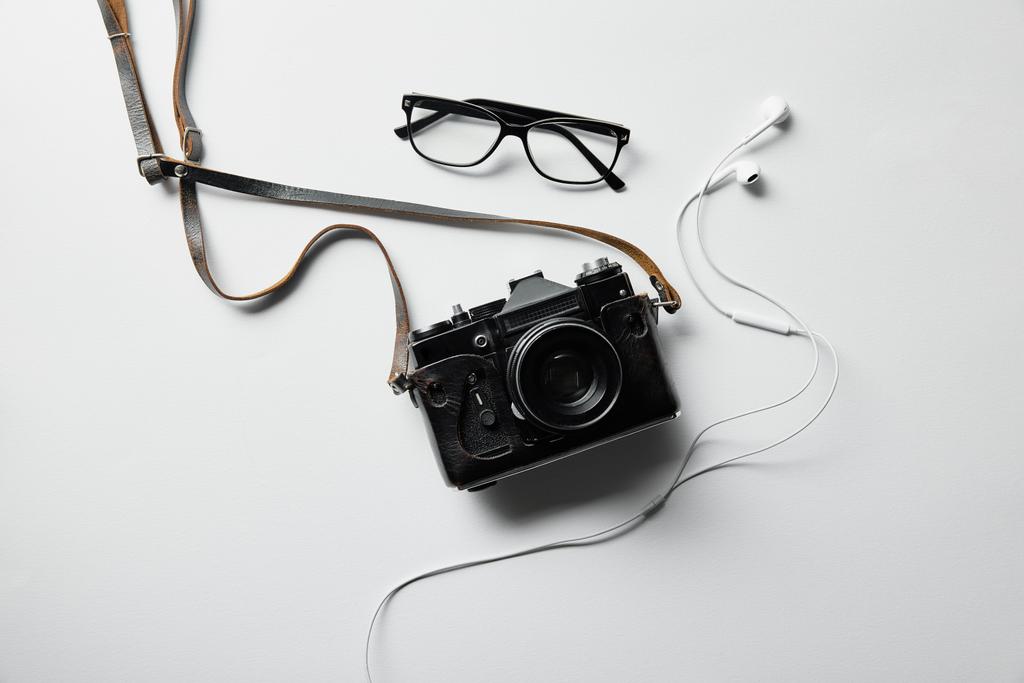 bovenaanzicht van oortelefoons, brillen en fotocamera op wit oppervlak - Foto, afbeelding