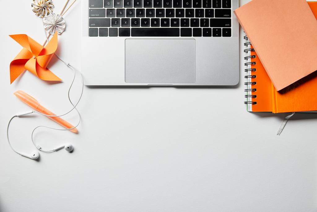 vista dall'alto di blocco note arancione, auricolari, penna e laptop su superficie bianca
 - Foto, immagini