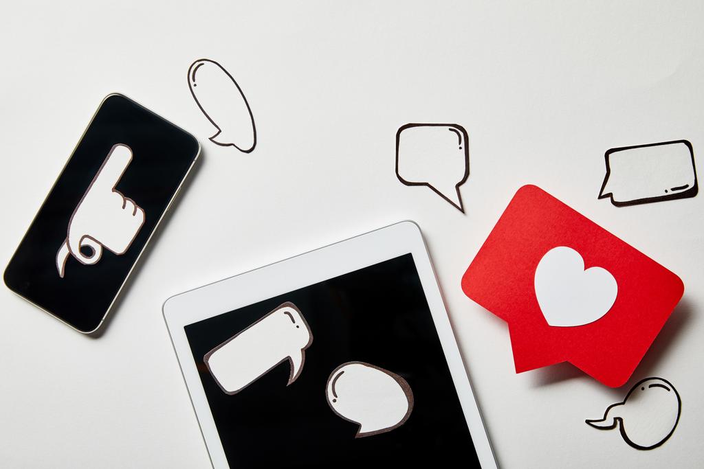 tableta digital y teléfono inteligente con burbujas de pensamiento y voz de papel, corazón de papel, tarjeta de apuntar en la superficie blanca
 - Foto, Imagen