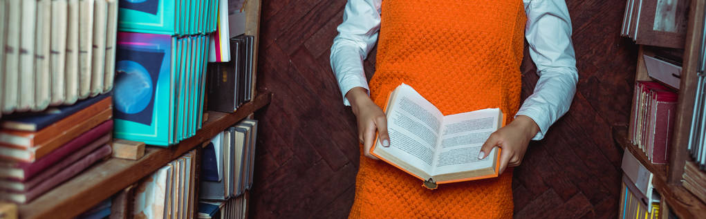 plan panoramique de la femme en robe orange tenant livre et couché sur le sol dans la bibliothèque
  - Photo, image