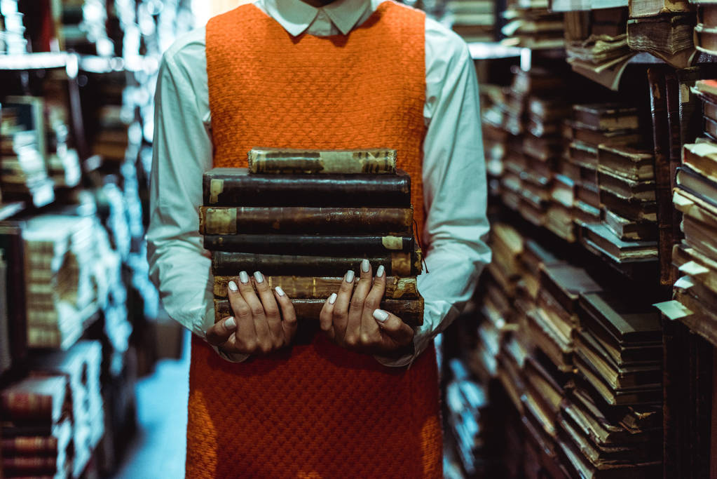 cropped view of woman in orange dress holding retro books in library  - Photo, Image