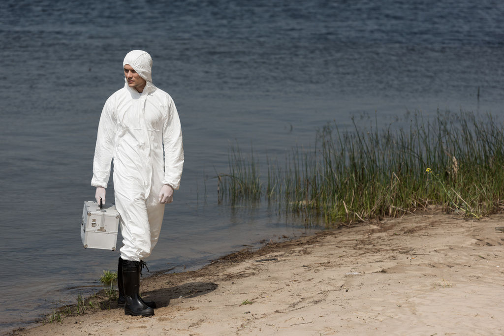 vue complète de l'inspecteur de l'eau en tenue de protection tenant le kit d'inspection et debout sur la côte de la rivière
 - Photo, image