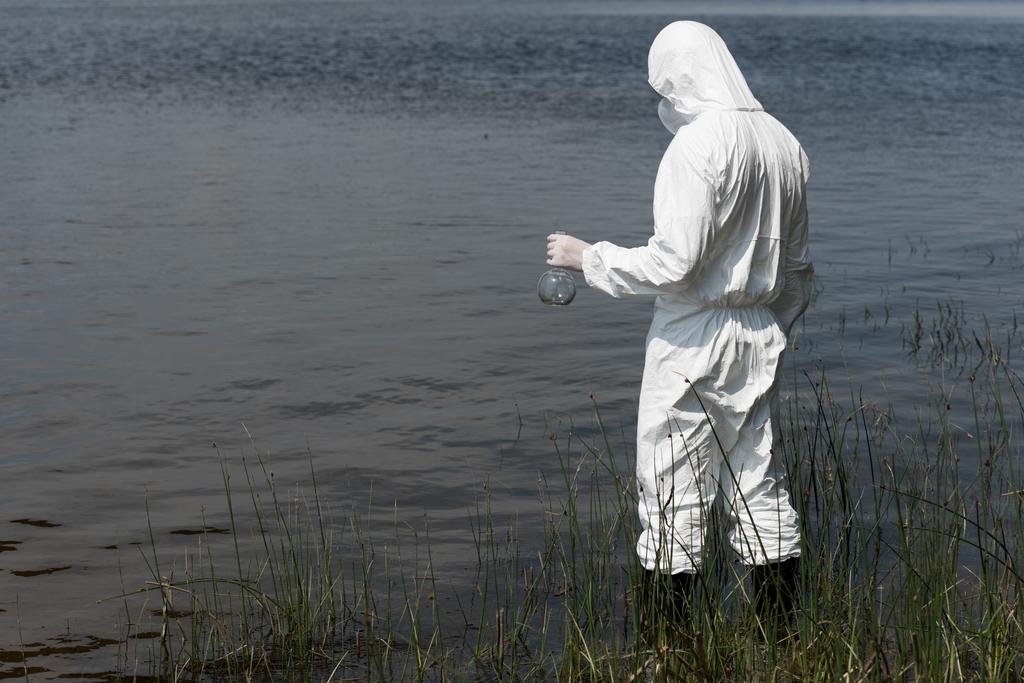 nehir kenarında dururken şişe tutan koruyucu kostüm su müfettişi - Fotoğraf, Görsel