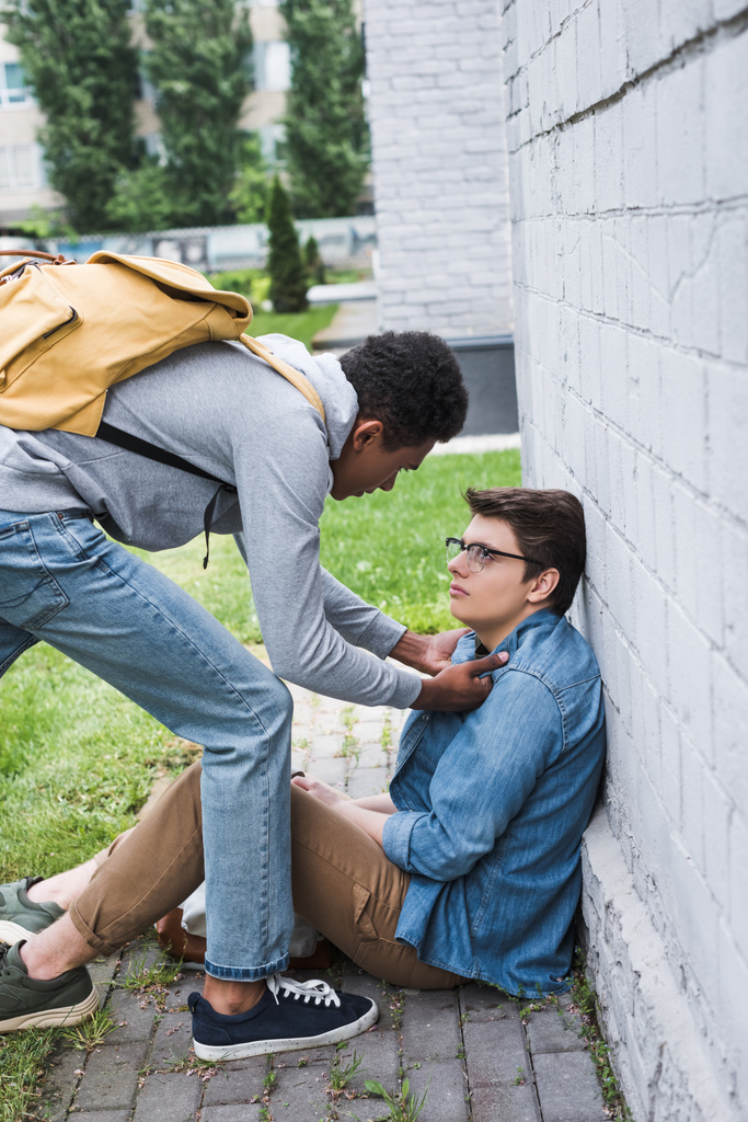 攻撃的でブルネットのアフリカ系アメリカ人の少年は、眼鏡でおびえた少年をいじめる  - 写真・画像