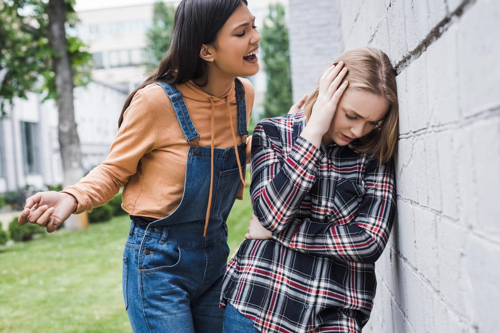 aggressive and brunette teenager screaming at blonde and scared teenager - Photo, Image